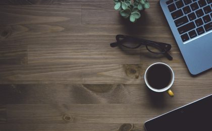 少女前线2常见问题清单被打印成纸质卡片铺在木桌上，旁边放着一支笔和一杯凉掉的茶，呈现资料整理工作的沉静状态